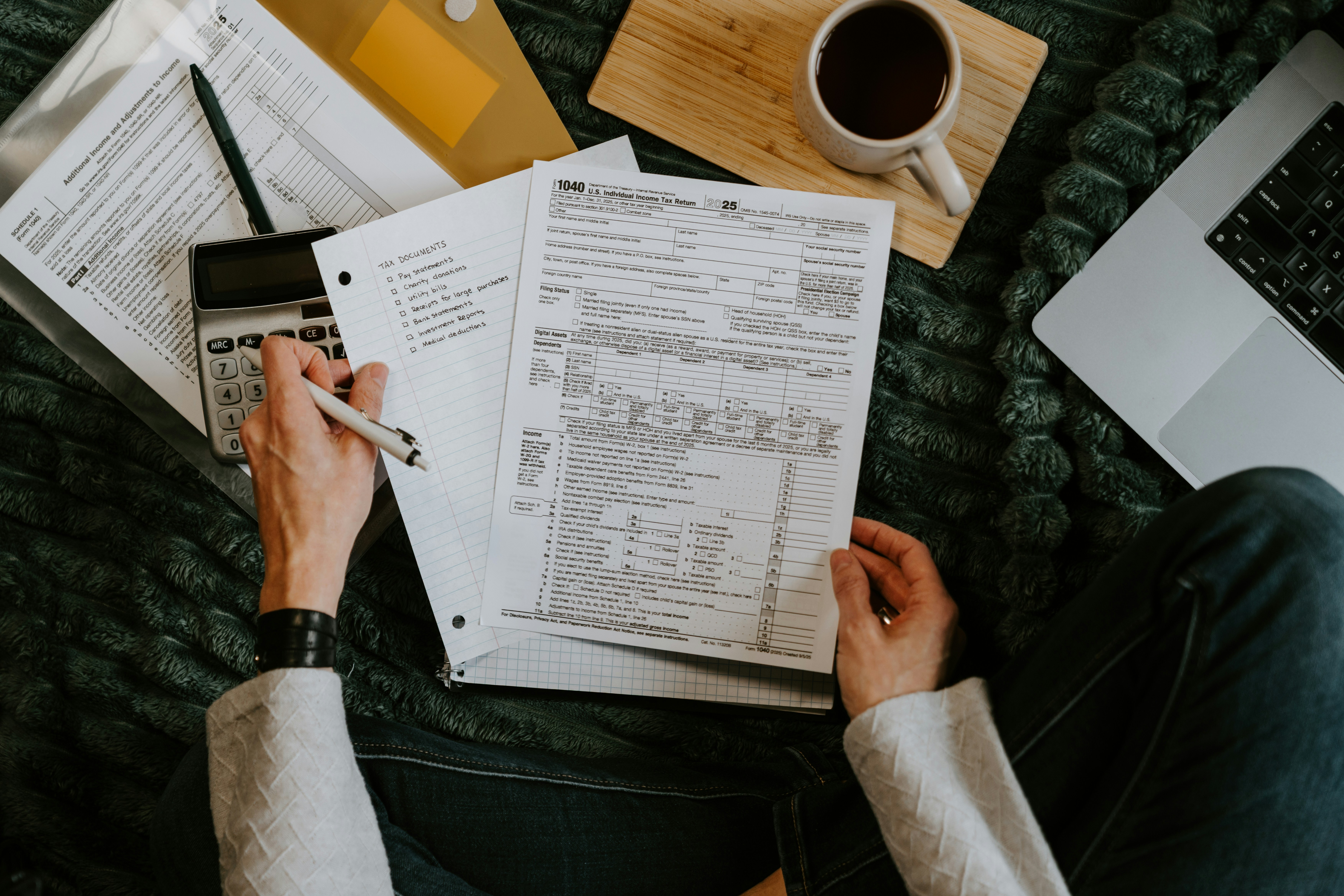 Person reviewing financial paperwork with a calculator and laptop.